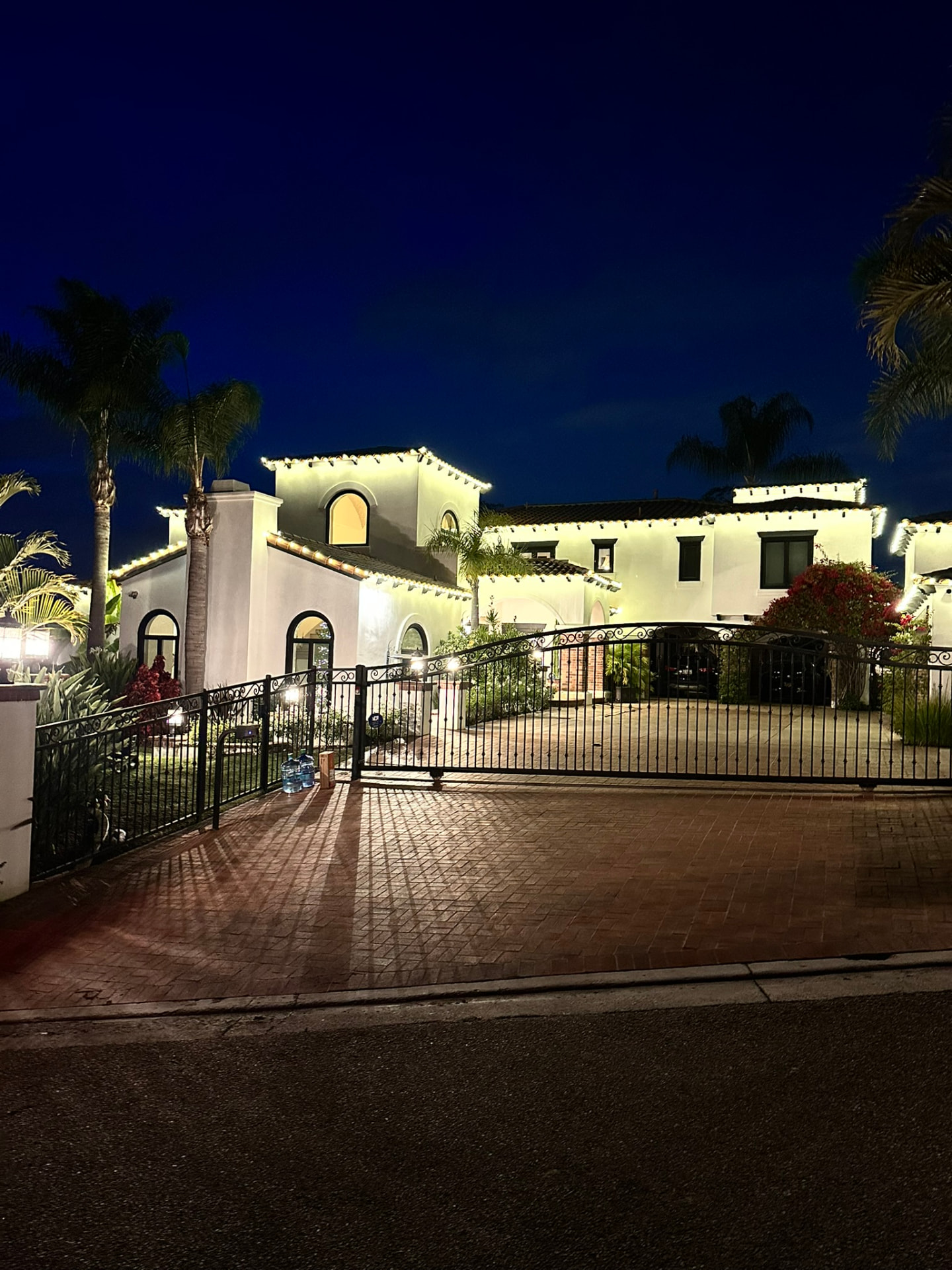 Large estate home at night with warm white C9 roofline lighting and palm trees